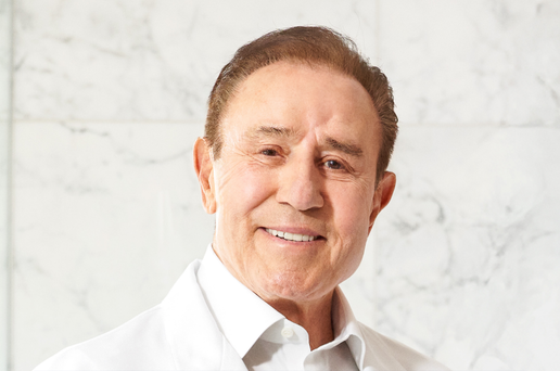 Dr. Vos, founder of Vos Collection, smiling in white shirt against marble wall - Vos Collection